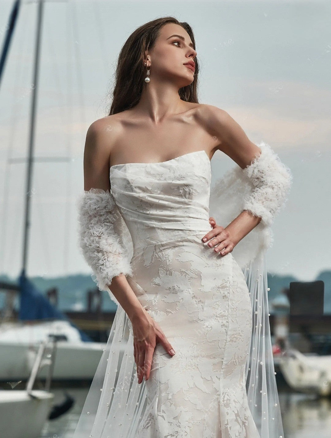 Woman in a white lace wedding dress with sheer sleeves by a marina.