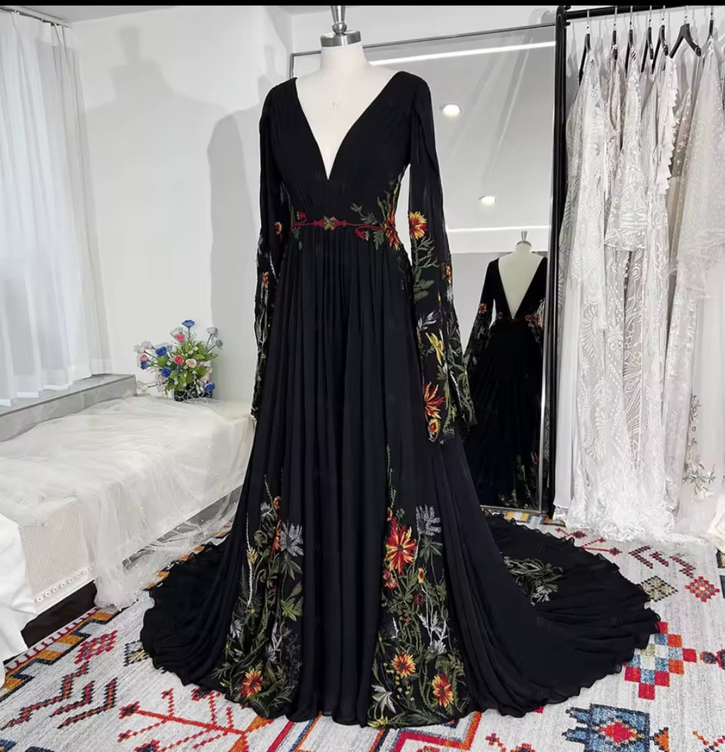 Black evening gown with floral embroidery on a mannequin in a room with white curtains and a colorful rug.
