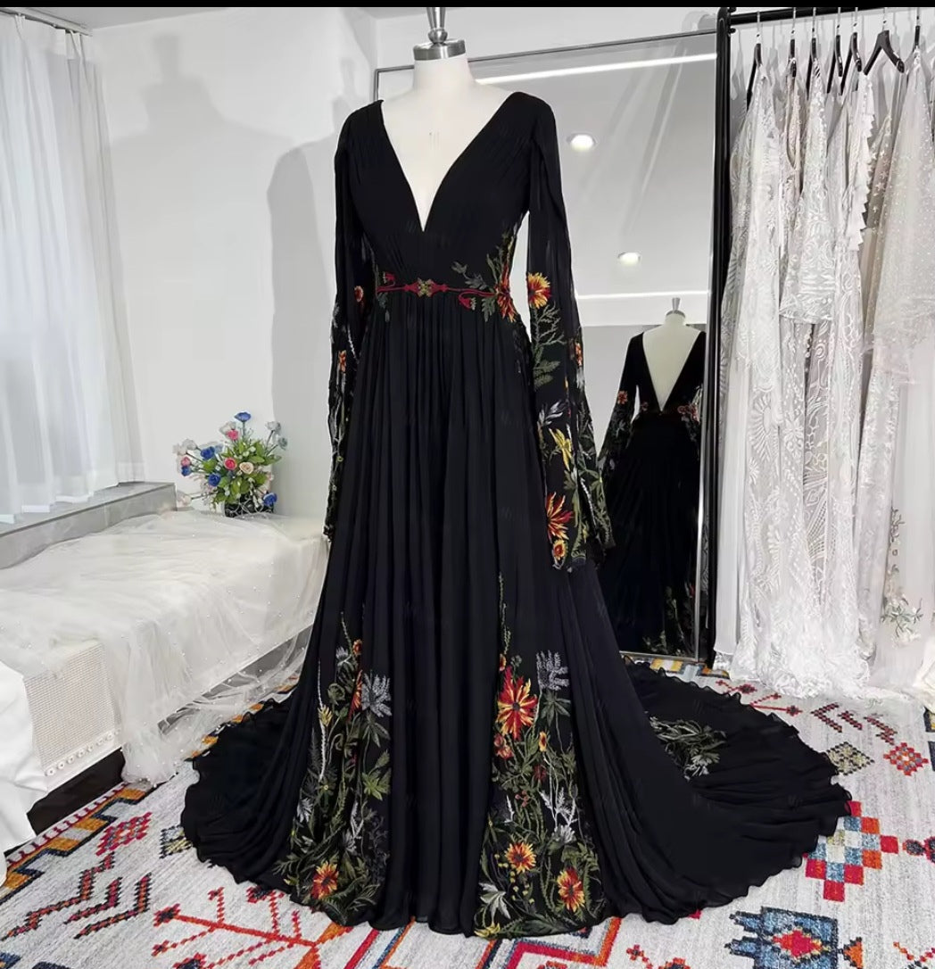 Black evening gown with floral embroidery on a mannequin in a room with white curtains and a colorful rug.