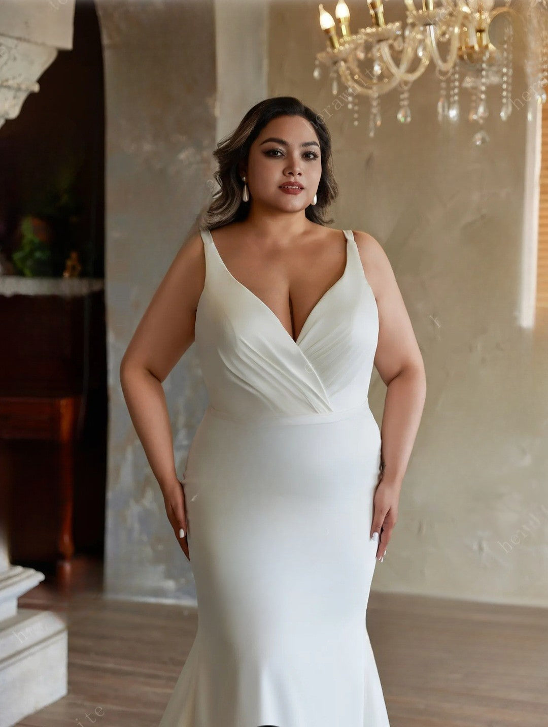 Woman in a white wedding dress standing in an elegant room with a chandelier.