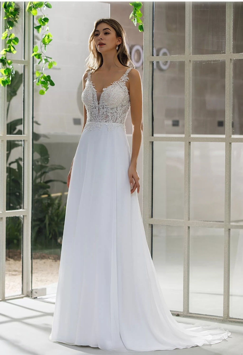 Woman wearing a white wedding dress with lace detailing in a bright indoor setting.