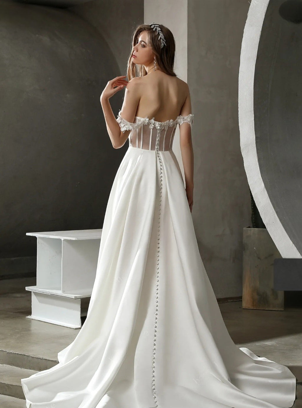 Woman wearing a white wedding dress with a long train in an indoor setting.