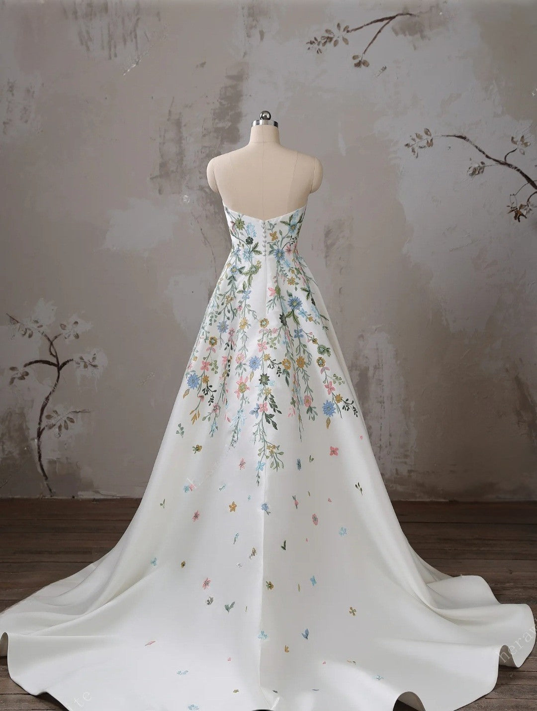 Floral-patterned gown on a mannequin against a textured wall.
