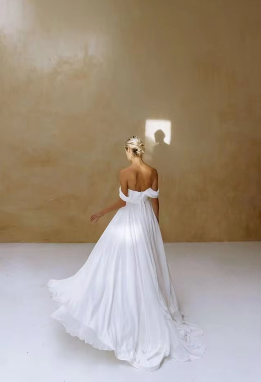 Woman in a white off-shoulder gown against a plain background
