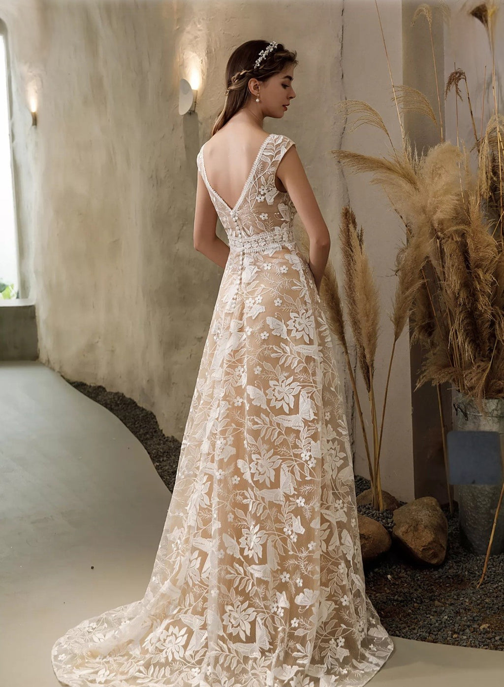 Woman in a long, elegant lace dress standing in a softly lit room with decorative elements.