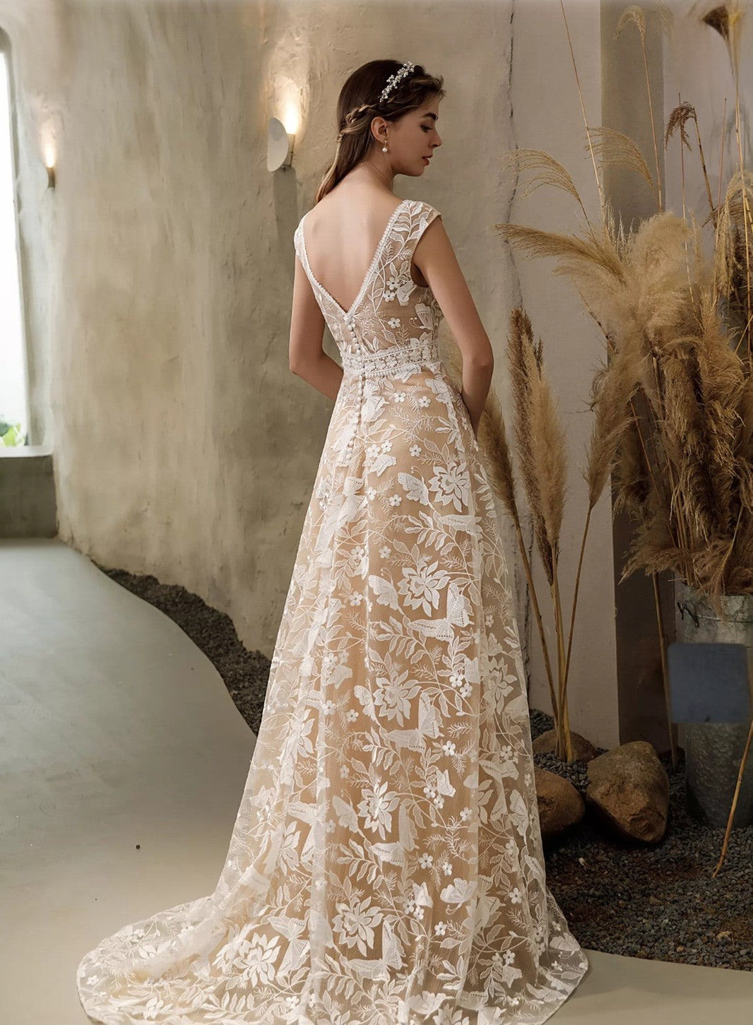 Woman in a long, elegant lace dress standing in a softly lit room with decorative elements.