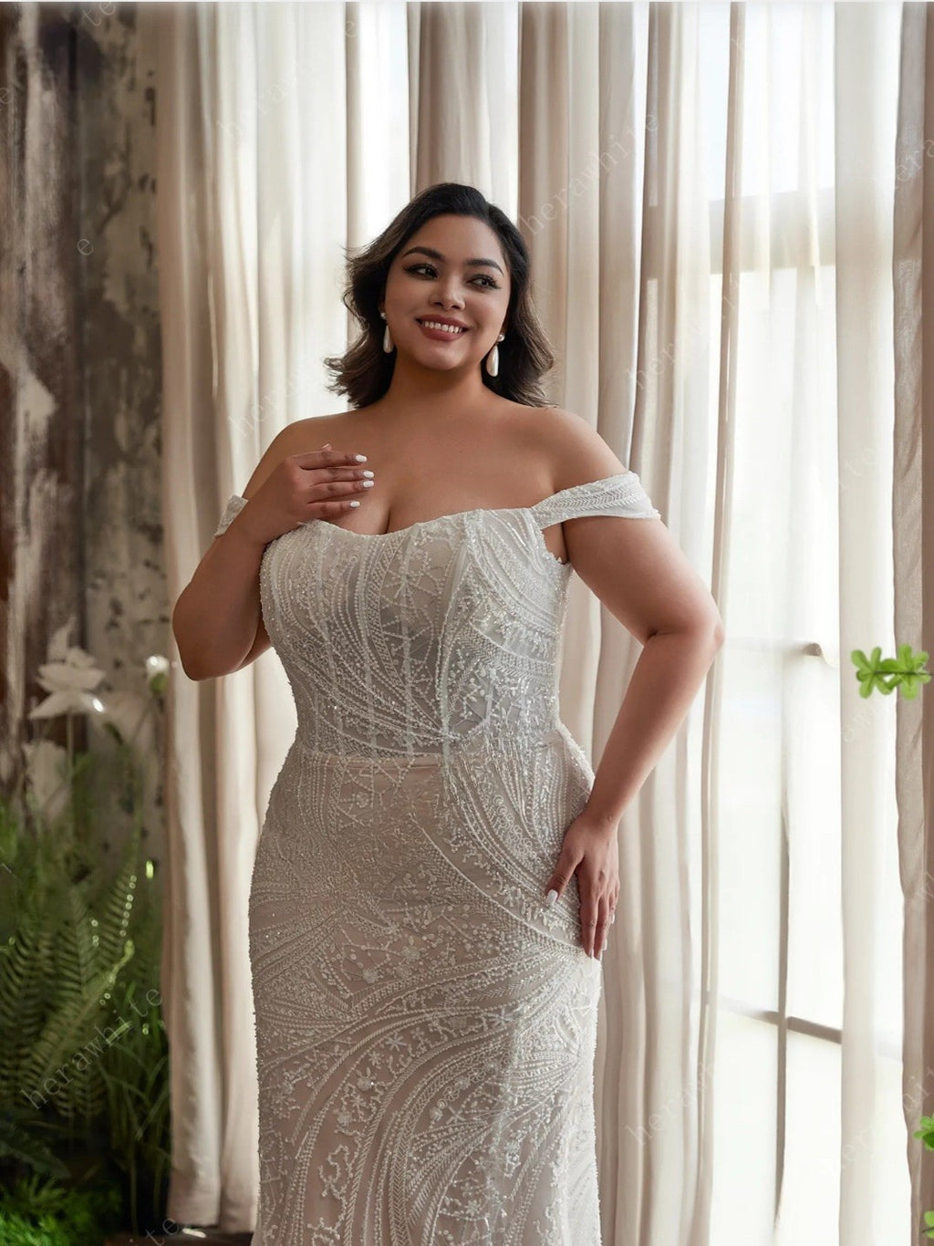 Woman wearing a white off-shoulder dress with intricate patterns in a softly lit room.