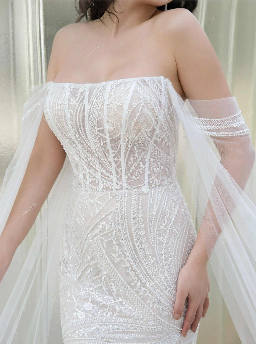 White off-shoulder dress with intricate detailing on a neutral background