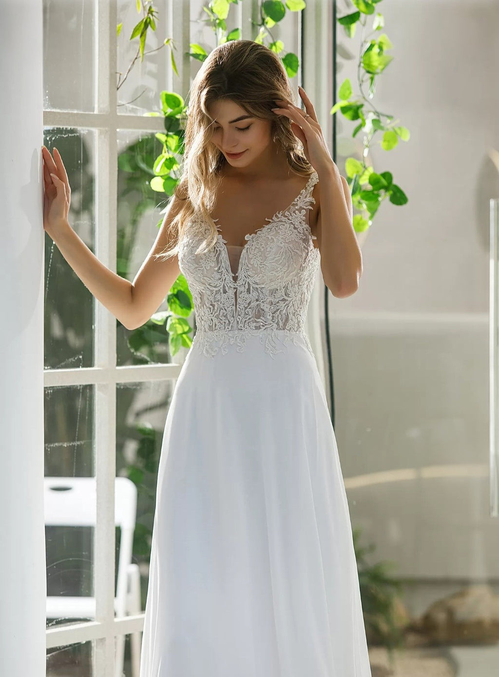 Woman wearing a white lace wedding dress in a bright room with plants.