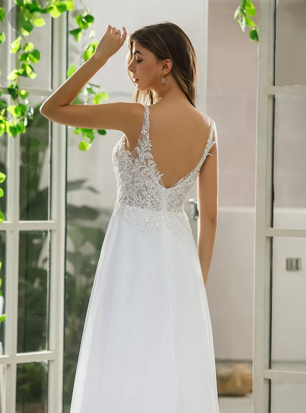 Woman wearing a white wedding dress with lace detailing in a softly blurred indoor setting.