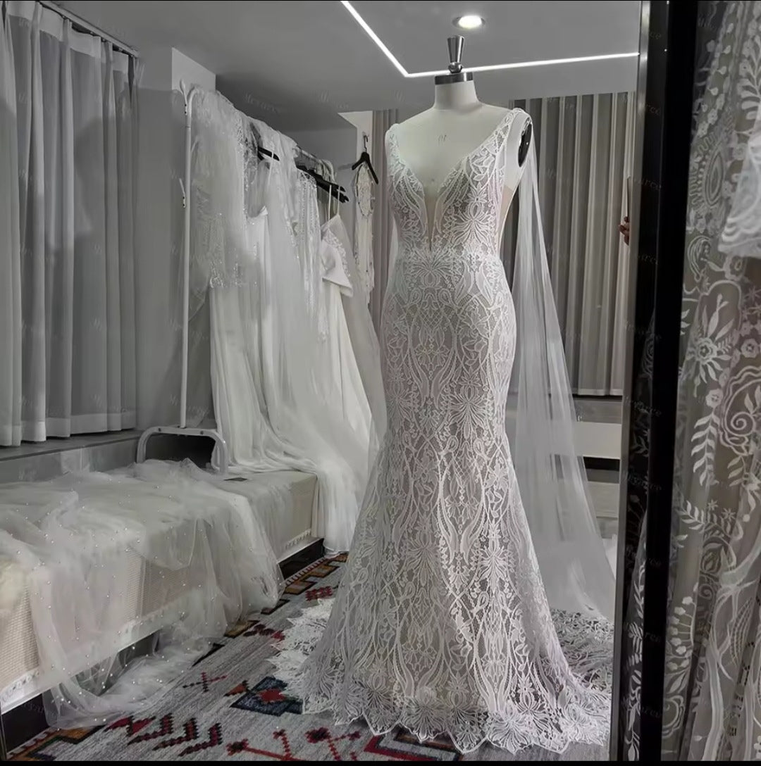 White lace wedding dress on a mannequin in a room with other wedding dresses.