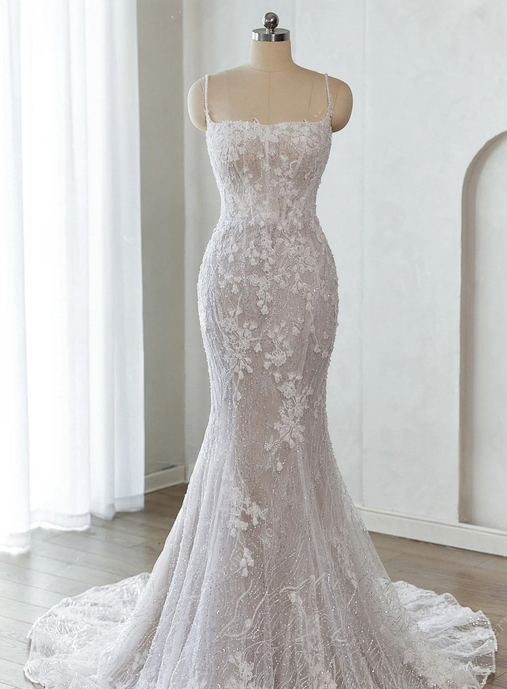 White lace wedding dress on a mannequin against a white curtain background