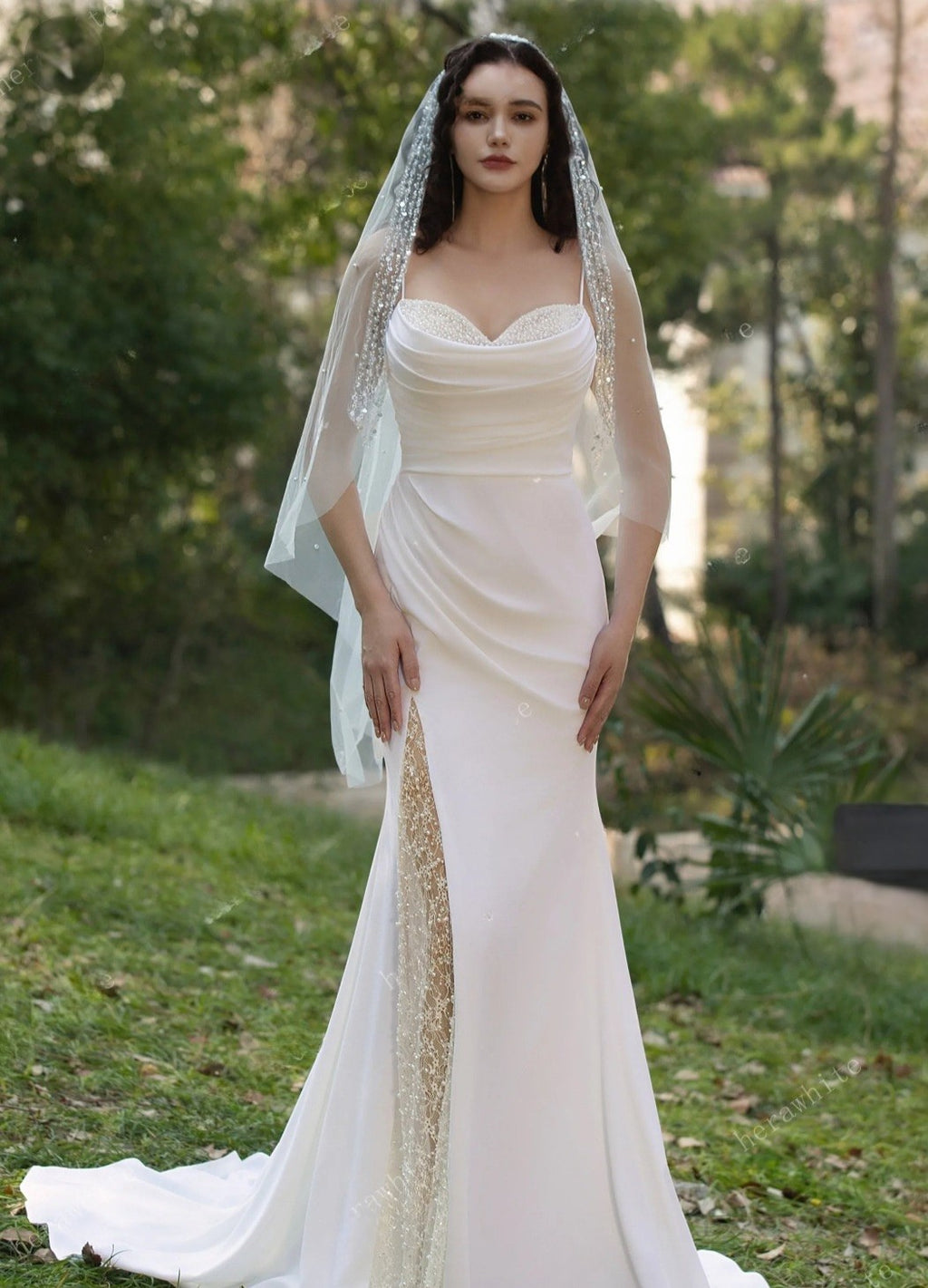 Woman in a white wedding dress with a veil standing outdoors.