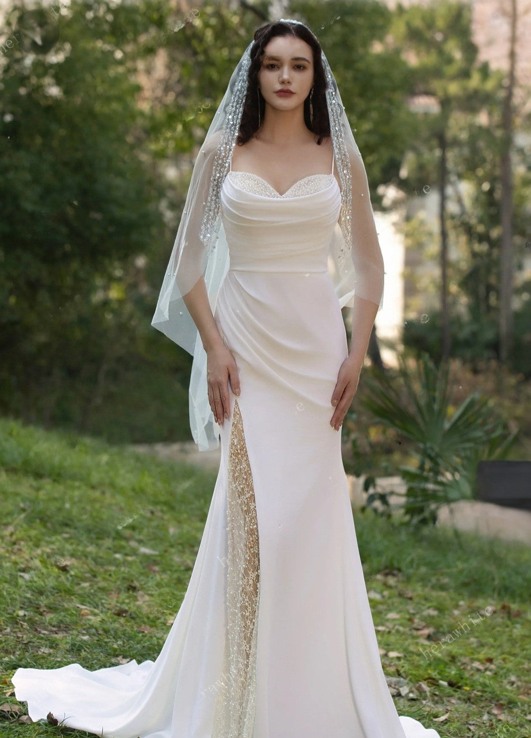 Woman in a white wedding dress with a veil standing outdoors.