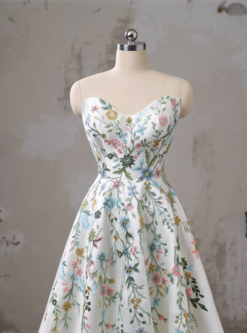 Floral dress on a mannequin against a textured wall.