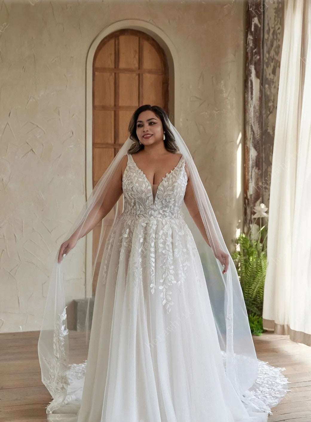 Woman in a white wedding dress with a long veil standing indoors.