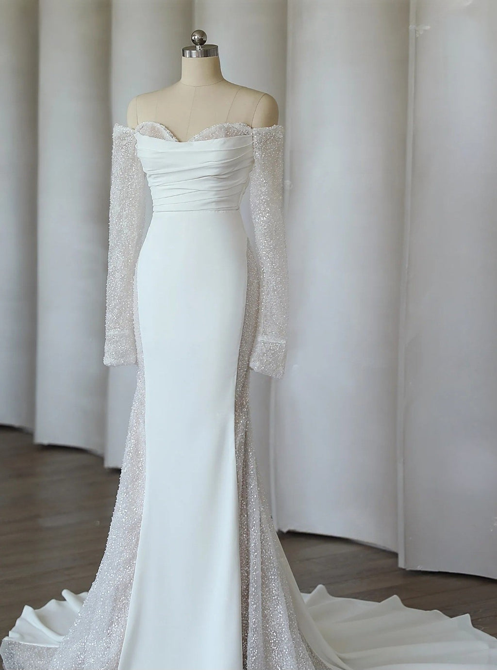 White off-shoulder gown with long sleeves on a mannequin against a neutral background