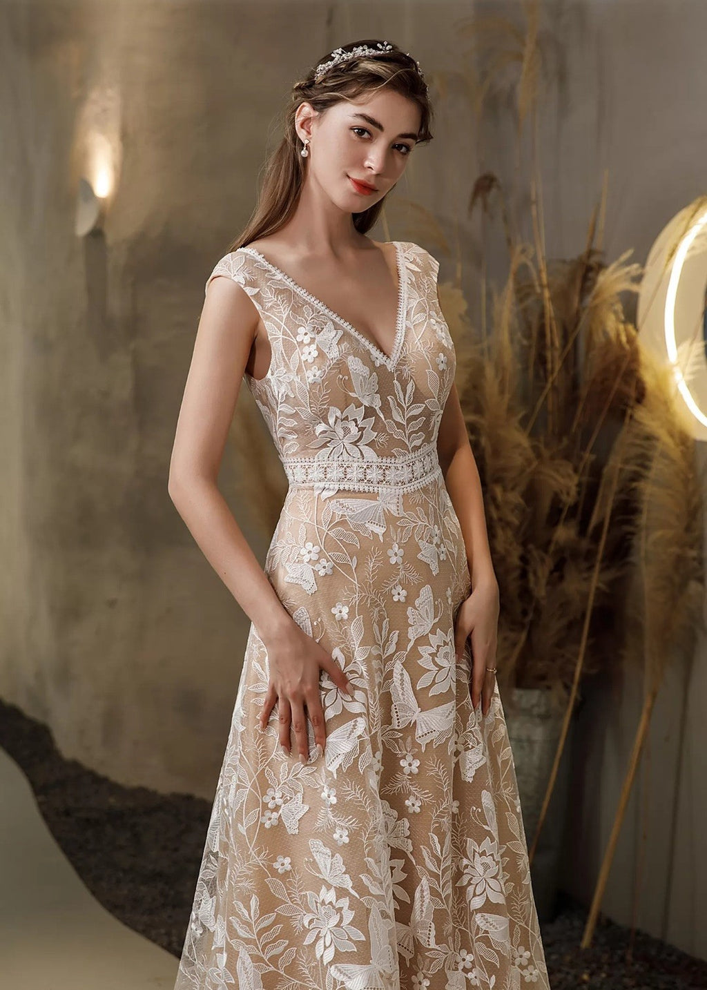 Woman wearing a beige lace dress with floral patterns in a warm-toned setting.