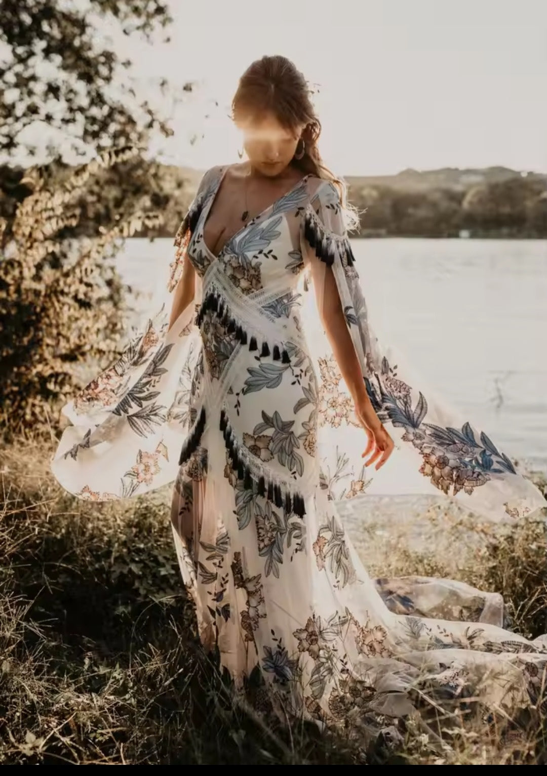 Woman in a floral dress standing by a body of water with a blurred background