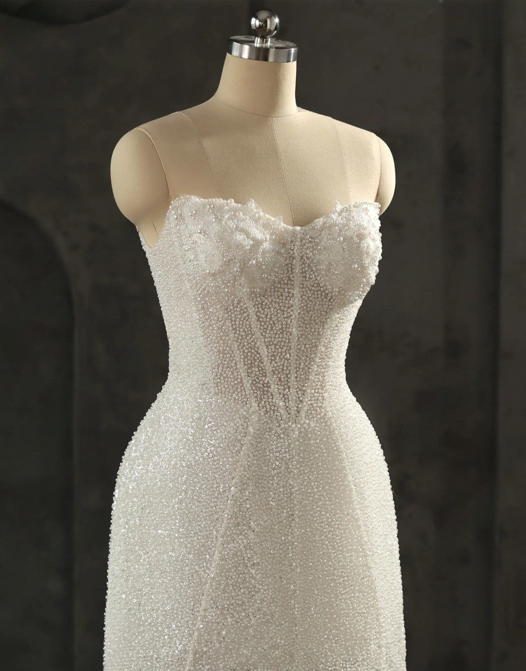 White beaded strapless dress on a mannequin against a dark background