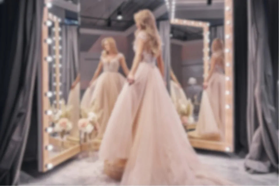 Woman trying on a light pink dress in front of a large vanity mirror with lights.